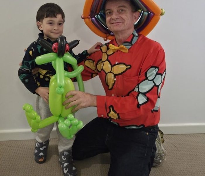 Adelaide Balloon Man wearing a colorful shirt and hat, posing alongside a young boy holding a green balloon dragon sculpture